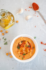 A bowl of delicious hummus with olive oil, garlic and paprika on a grey background.