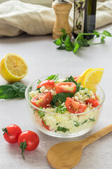 Fresh home-made tabouli, or tabbouleh salad, with its ingredients, side view on grey background