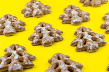 Christmas tree cookies on yellow background. New Year's food. Festive baked goods. Gingerbread on the table. Icing sugar sweetness taste season. Pattern