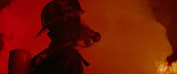 Dramatic silhouette of American firefighter in full gear exploring the huge fire zone © supamotion