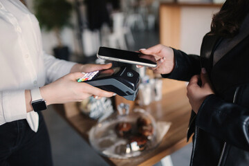 Closeup of female paying with smartphone during Covid-19 pandemic. Cashier hand holding credit card reader machine while client holding phone for NFC payment