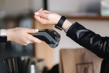 Female customer making wireless or contactless payment using smartwatch. Closeup of human hands during payment. Store worker accepting payment over nfc technology - Powered by Adobe