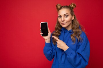 Photo of beautiful smiling young woman good looking wearing casual stylish outfit standing isolated on background with copy space holding smartphone showing phone in hand with empty screen display for
