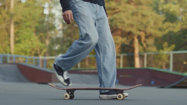 Slowmo shot with low-section of unrecognizable teenager in jeans walking past camera and picking up his skateboard with nose pick-up trick