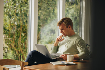 Man at home looking at laptop and thinking
