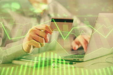 Double exposure of man hands holding a credit card and Forex graph drawing. Stock trading and digital fintech in Internet E-commerce concept.