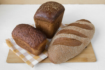 A lot of different bread lies on a wooden board on a light background, rye, whole grain, with seeds, minimalism