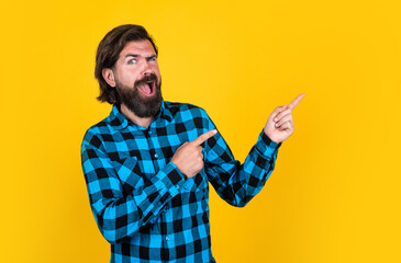 Portrait of a surprised man with moustache pointing finger away on a yellow background, announcement