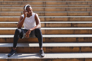 African american athlete man sitting outside on stair with headphone listening relaxation after exercis relax, relaxation sport concept.