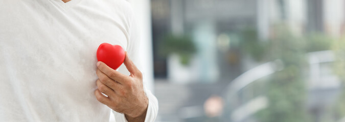 Man holding red heart in hand attach chest. Happy health concept. crop image banner size.
