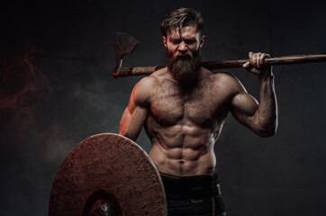Frenzied viking in dark background with axe and shield - obrazy, fototapety, plakaty