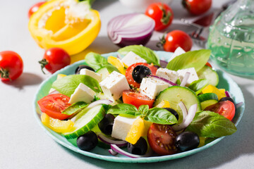 Fresh homemade greek salad with basil leaves on a plate and ingredients for cooking on the table. Domestic life. Hard light