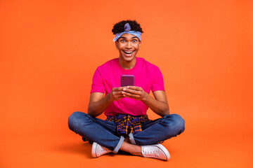 Full length body size photo of amazed guy reading news with cellphone laughing isolated vibrant orange color background