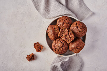 Homemade chocolate cupcakes in bowl with napkin on wooden light background, top view, copy space