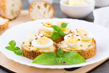 Hearty breakfast in the morning. Fresh baguette sandwiches with butter, quail eggs, flax seeds and basil seeds on a plate. Close-up