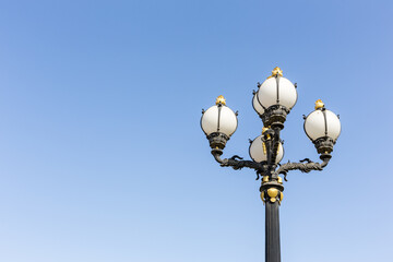 Vingate style street lamp with golden ornaments and round bulbs against clear blue sky, Dubai, United Arab Emirates.