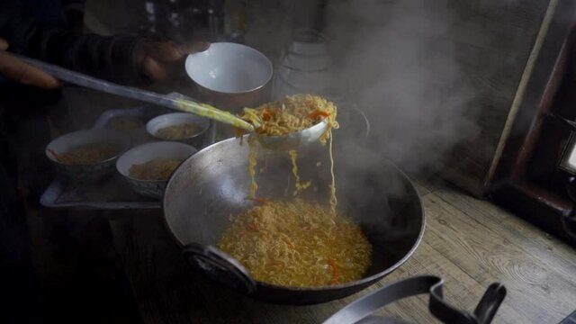 Person serves hot chowmin or noodles in a bowl in rural kitchen, slow motion
