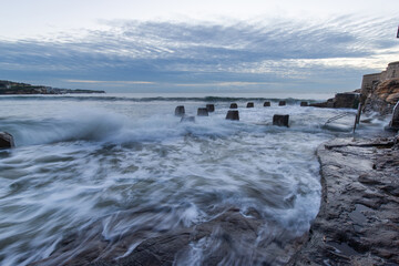 Wave coming over Coogee Beach coastline on cloudy morning.