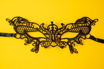 Beautiful black lace mask isolated on yellow background. Sexy black eyes mask. Party lace mask. Venetian mask for girls