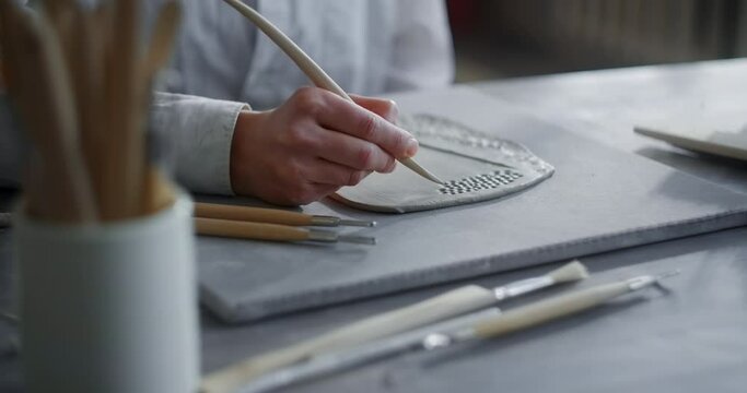Ceramist carves a pattern on a raw clay, potter makes texured clay surface, making the ceramics at the pottery workshop, 4k 60p Prores HQ 10 bit