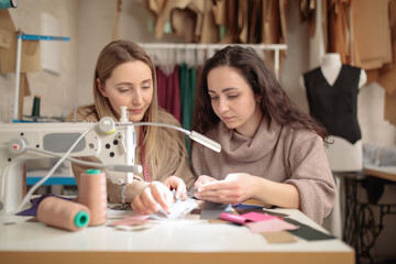 two femail Dressmakers or tailors or fashiondesigners or seamstresses working with sewing machine atv workshop studio.