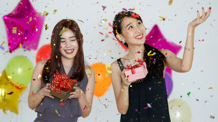 Delighted Asian girlfriends standing under confetti