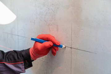 A man, an electrician marks out holes for sockets with a pencil, a tape measure