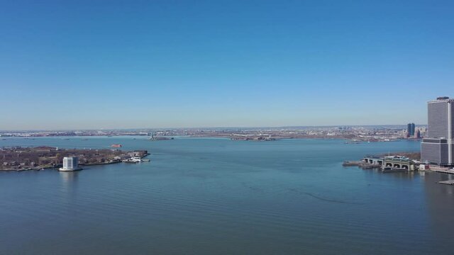 An aerial view the east East River on a sunny day with blue skies. The drone camera, facing lower Manhattan, pan left towards Governor's Island and Brooklyn Heights.
