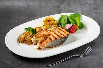 plate of grilled salmon steak with vegetables on dark stone table