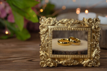 Two golden wedding rings close up with wooden picture frame on wooden background. Wedding invitation card concept. 