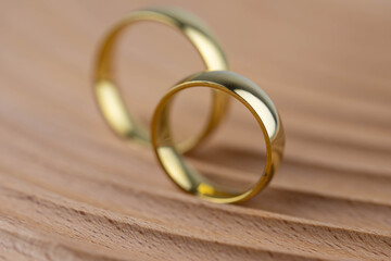 Two golden wedding rings close up on natural wooden background. Eco wedding invitation card concept. 