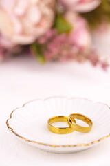 Two golden wedding rings close up with flowers on white background. Wedding invitation card concept. 