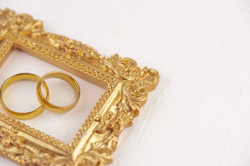 Two golden wedding rings close up with wooden picture frame on white background. Wedding invitation card concept. 