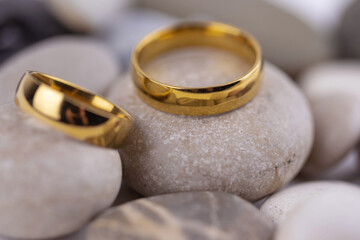 Two golden wedding rings close up on gray pebble stones. Wedding on the beach invitation card concept.