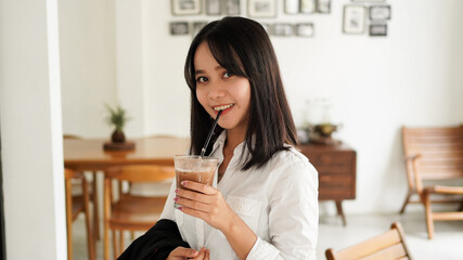 Beautiful young asian businesswoman in suit standing holding brown coffee cup in caffe while having a coffee break.