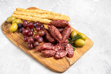 Traditional Italian antipasti salami on a wooden plate, served with olives and grapes. Food for an aperitif and dinner lunch in the restaurant. 