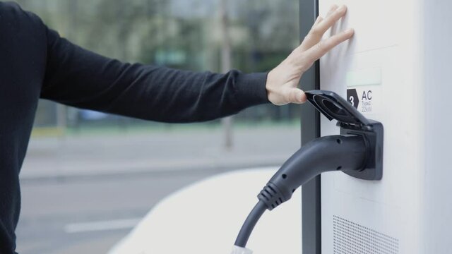 Woman connecting charging plug to electric vehicle charging station
