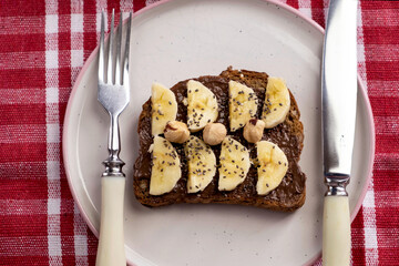 Toasted whole wheat bread with chocolate nuts paste nutella topping, banana, chia seeds, almonds and hazelnuts toast. Healthy proper nutrition for breakfast