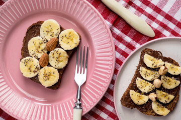 Toasted whole wheat bread with chocolate nuts paste nutella topping, banana, chia seeds, almonds and hazelnuts toast. Healthy proper nutrition for breakfast