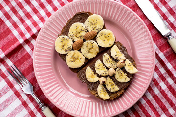 Toasted whole wheat bread with chocolate nuts paste nutella topping, banana, chia seeds, almonds and hazelnuts toast. Healthy proper nutrition for breakfast