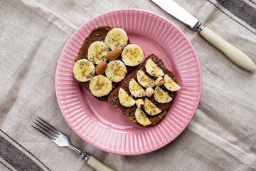 Toasted whole wheat bread with chocolate nuts paste nutella topping, banana, chia seeds, almonds and hazelnuts toast. Healthy proper nutrition for breakfast