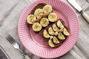 Toasted whole wheat bread with chocolate nuts paste nutella topping, banana, chia seeds, almonds and hazelnuts toast. Healthy proper nutrition for breakfast