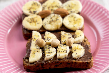 Toasted whole wheat bread with chocolate nuts paste nutella topping, banana, chia seeds, almonds and hazelnuts toast. Healthy proper nutrition for breakfast