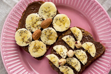 Toasted whole wheat bread with chocolate nuts paste nutella topping, banana, chia seeds, almonds and hazelnuts toast. Healthy proper nutrition for breakfast