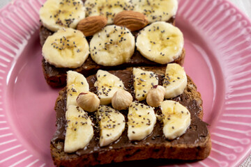Toasted whole wheat bread with chocolate nuts paste nutella topping, banana, chia seeds, almonds and hazelnuts toast. Healthy proper nutrition for breakfast