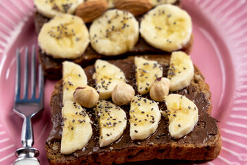 Toasted whole wheat bread with chocolate nuts paste nutella topping, banana, chia seeds, almonds and hazelnuts toast. Healthy proper nutrition for breakfast