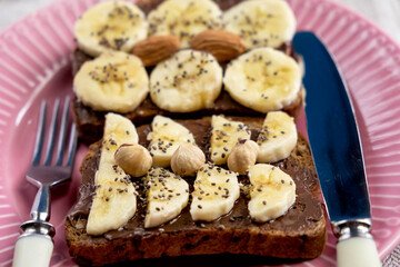 Toasted whole wheat bread with chocolate nuts paste nutella topping, banana, chia seeds, almonds and hazelnuts toast. Healthy proper nutrition for breakfast