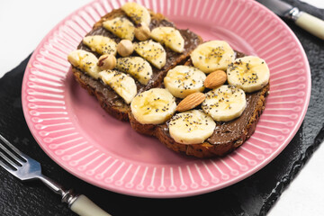 Toasted whole wheat bread with chocolate nuts paste nutella topping, banana, chia seeds, almonds and hazelnuts toast. Healthy proper nutrition for breakfast
