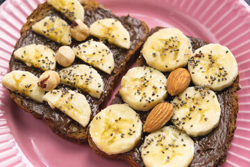 Toasted whole wheat bread with chocolate nuts paste nutella topping, banana, chia seeds, almonds and hazelnuts toast. Healthy proper nutrition for breakfast