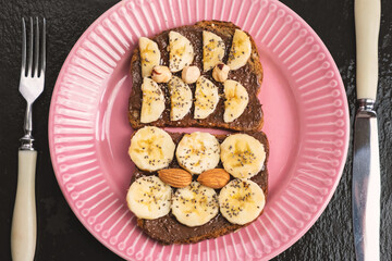 Toasted whole wheat bread with chocolate nuts paste nutella topping, banana, chia seeds, almonds and hazelnuts toast. Healthy proper nutrition for breakfast